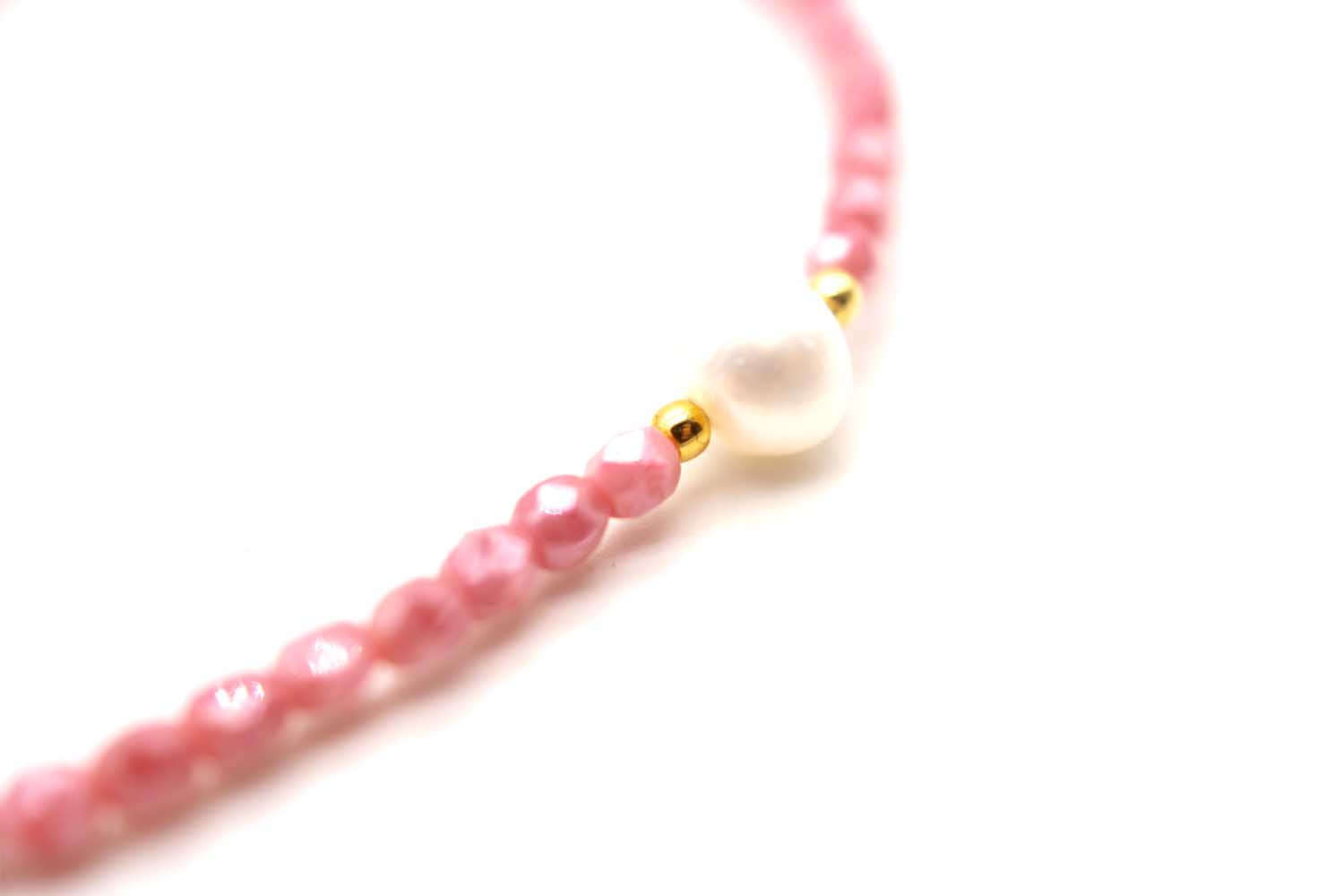 Nahaufnahme der weißen Süßwasserperle zwischen rosa Perlen und goldfarbenem Perlchen
