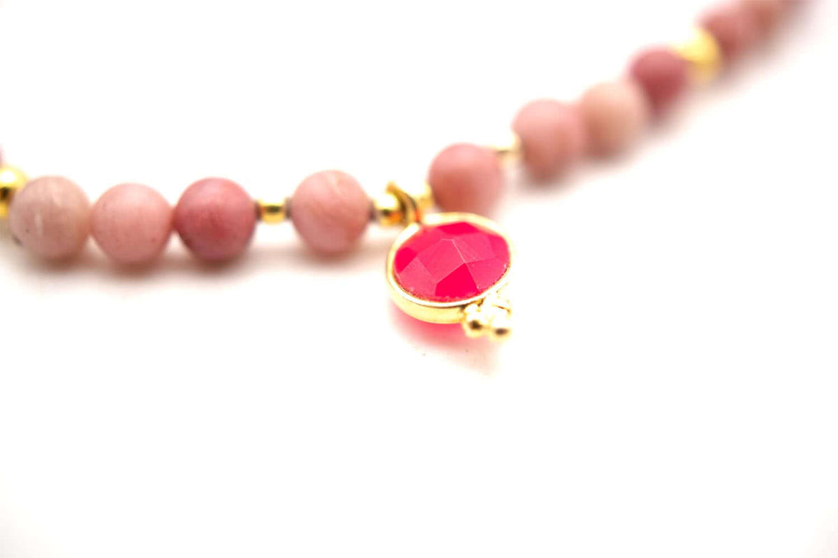 Nahaufnahme des runden, pink funkelnden Chalcedon-Anhängers in goldfarbener Fassung