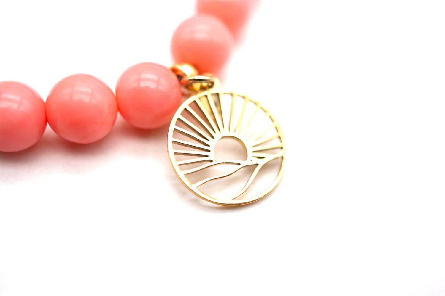 Nahaufnahme des goldfarbenen Sonnenmotiv-Anhängers an glänzend rosa Korallenperlen