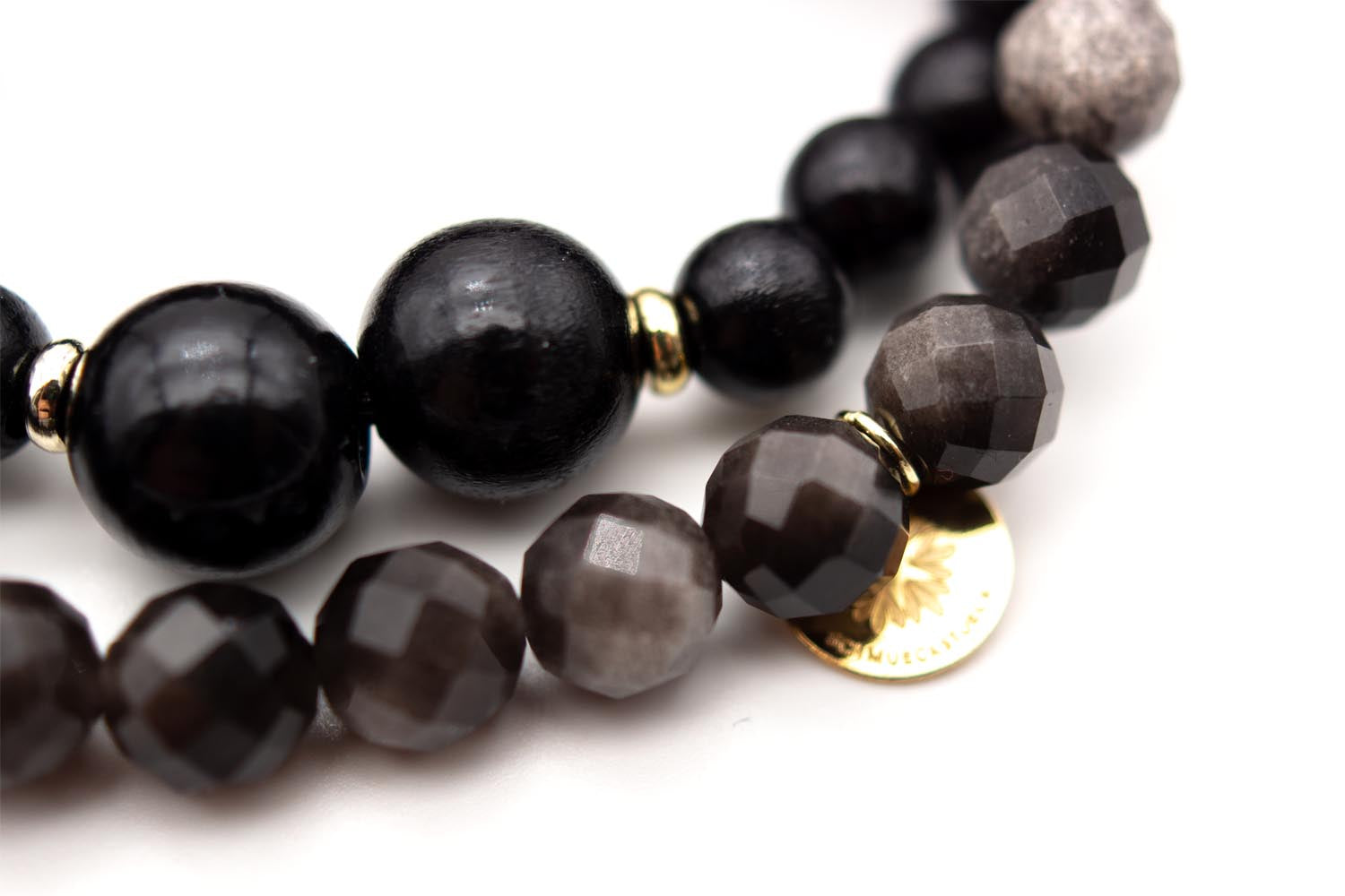 Detailansicht der glänzenden Holzperlen und facettierten grau-schwarzen Obsidian-Perlen mit goldfarbenem Logo-Plättchen