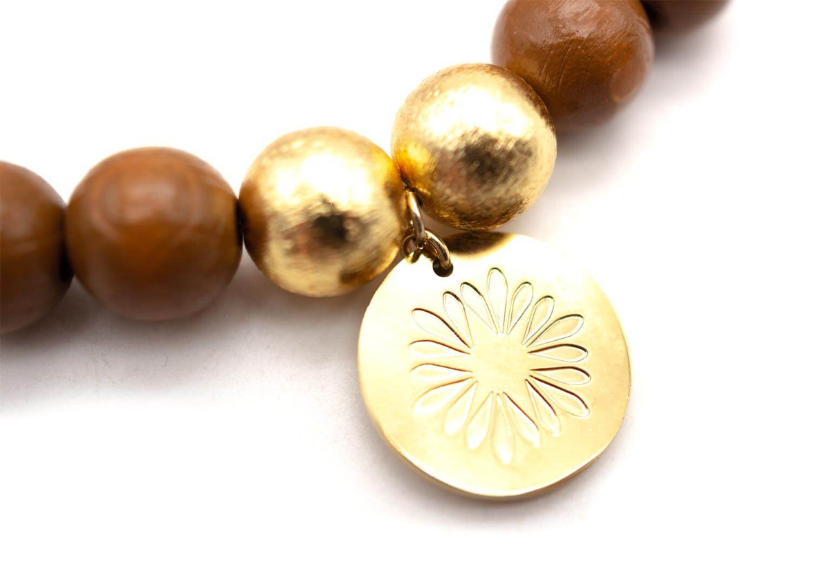 Nahaufnahme des vergoldeten Logo-Tags mit Blütenmuster zwischen den goldfarbenen Perlen