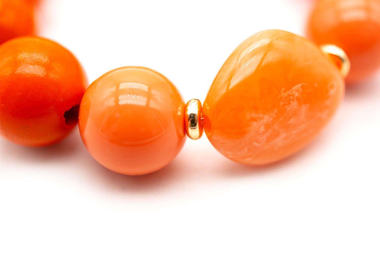 Detailaufnahme zweier glänzender orangefarbener Perlen mit vergoldetem Zwischenteil