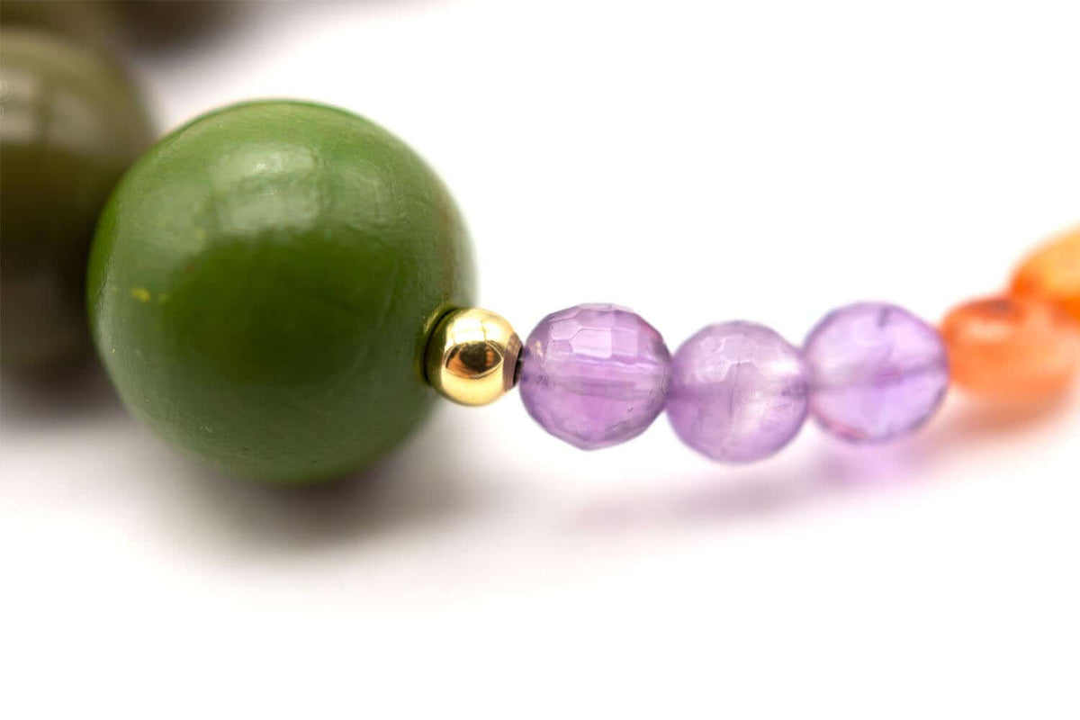 Detail der großen olivgrünen Perle neben facettierten violetten Edelsteinen und goldfarbener Perle