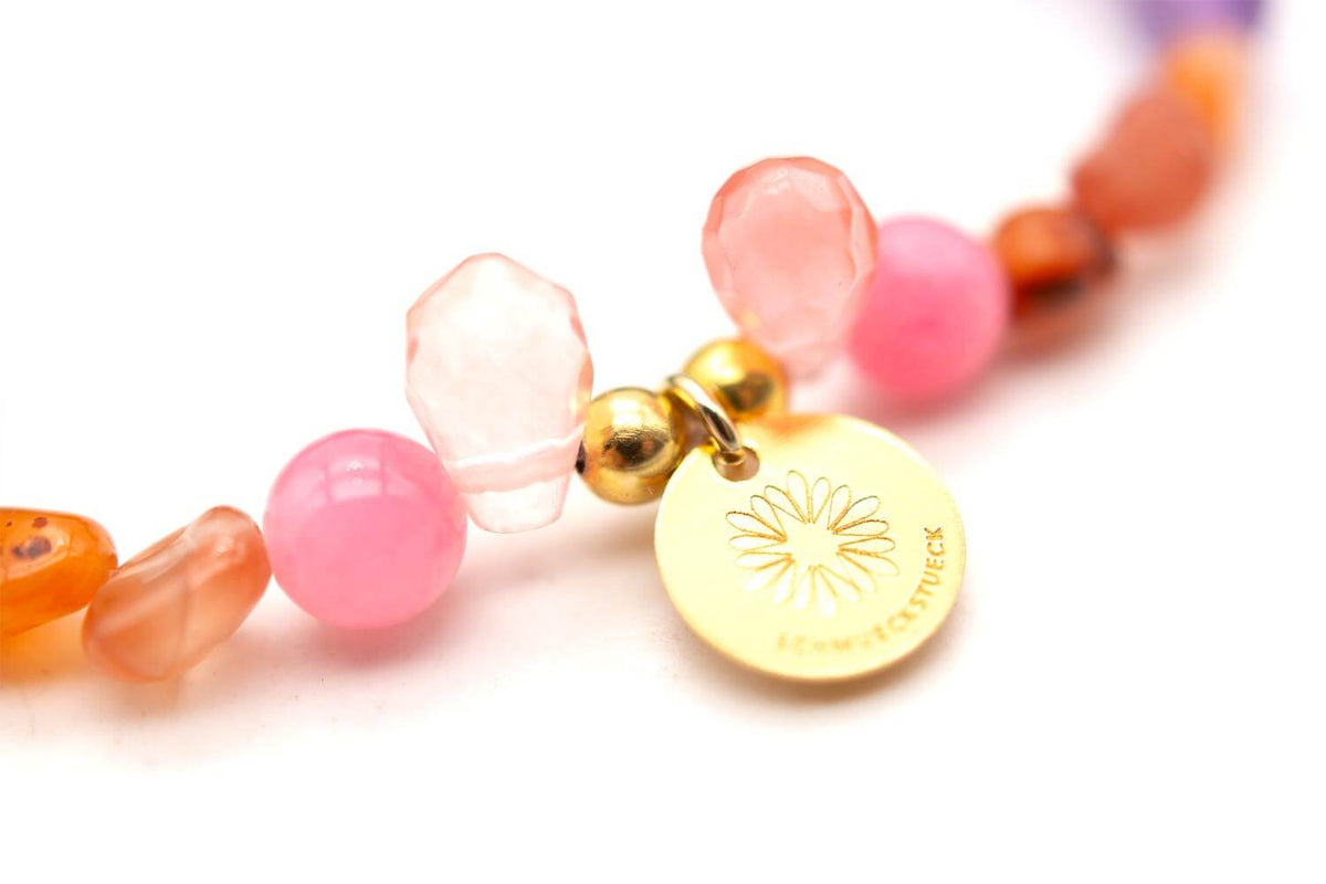 Nahaufnahme des vergoldeten runden Anhängers zwischen rosa und orangefarbenen Perlen