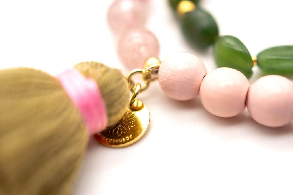 Detail der Quaste mit rosa Wicklung und rundem, vergoldetem Anhänger neben den Perlen