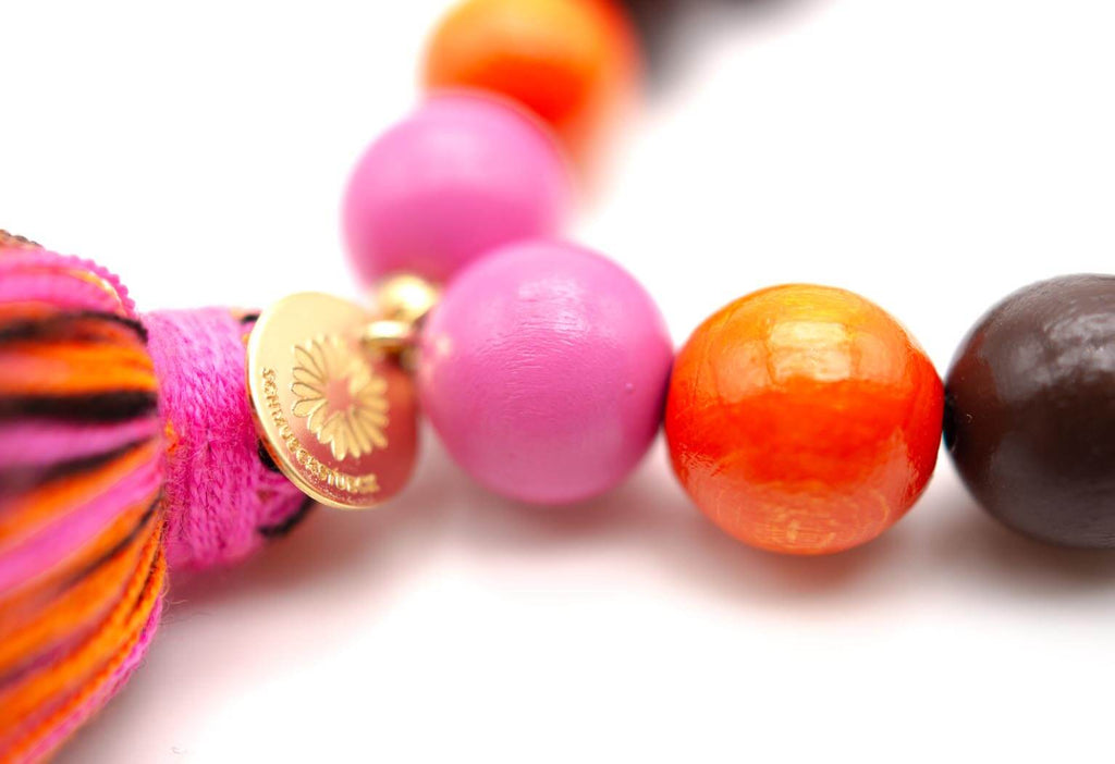 Detail der pink und orangefarbenen Holzperlen mit gravierter goldfarbener Plakette und mehrfarbiger Quaste