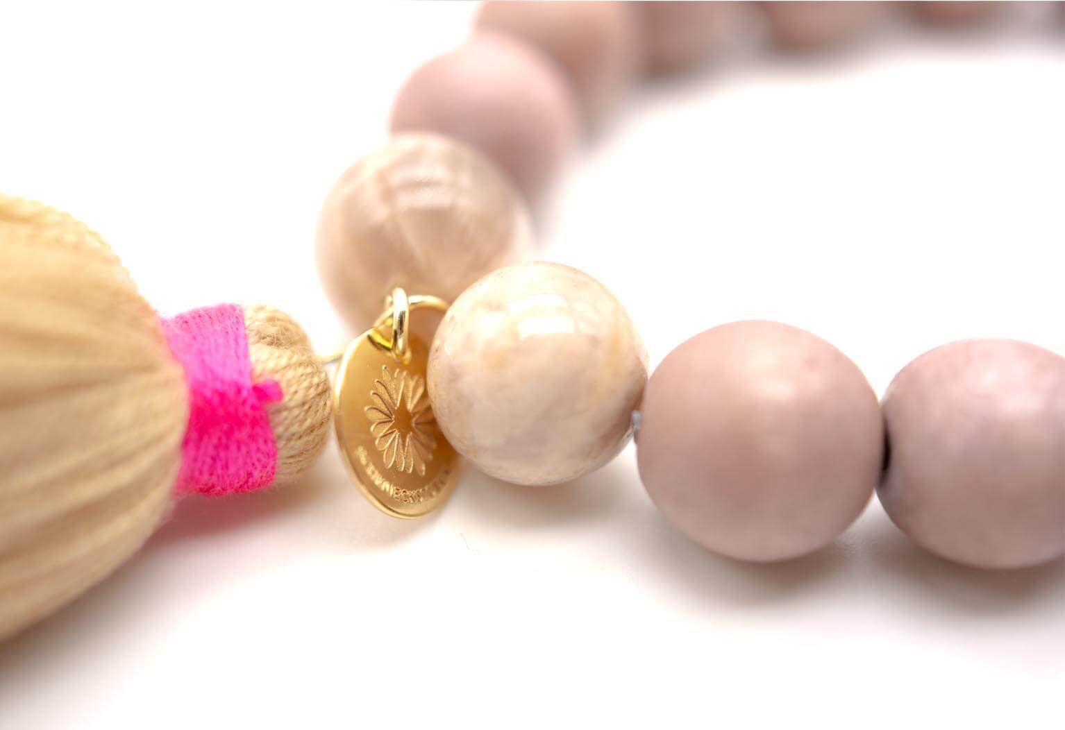 Nahaufnahme der Sonnenstein-Perle, der pink umwickelten Quaste und des goldfarbenen Markenplättchens