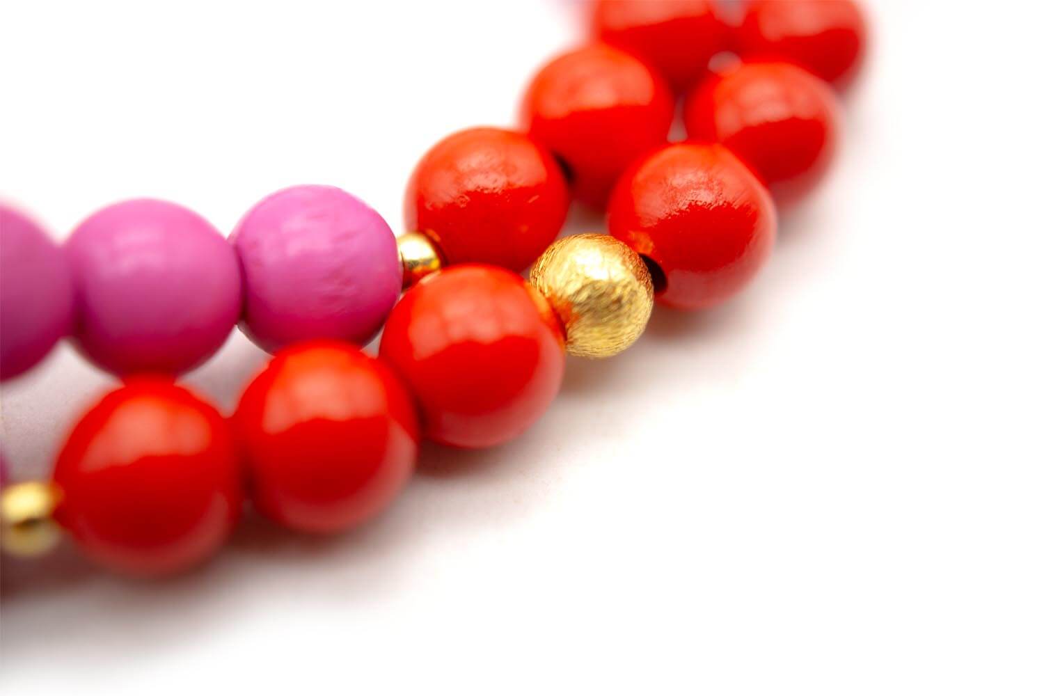 Nahaufnahme einer vergoldeten Perle zwischen den pink und rot glänzenden Holzperlen
