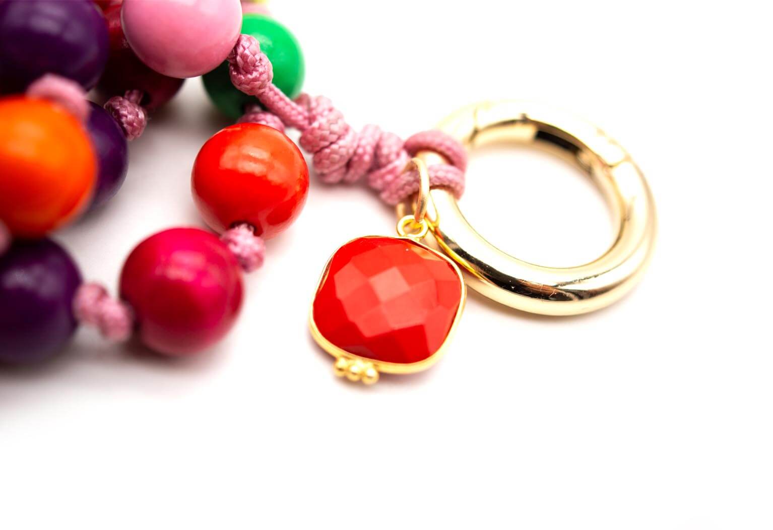 Detail des roten Koralle-Anhängers und goldfarbenen Rings am geflochtenen Band