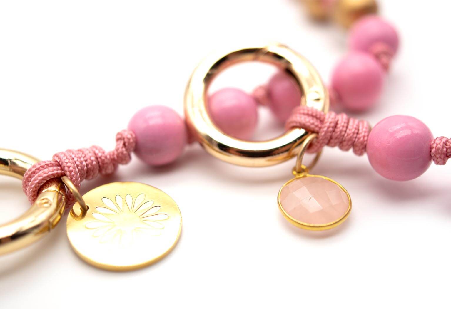 Detailansicht der goldfarbenen Ringe mit Logo-Münze und facettiertem Rosenquarz-Anhänger