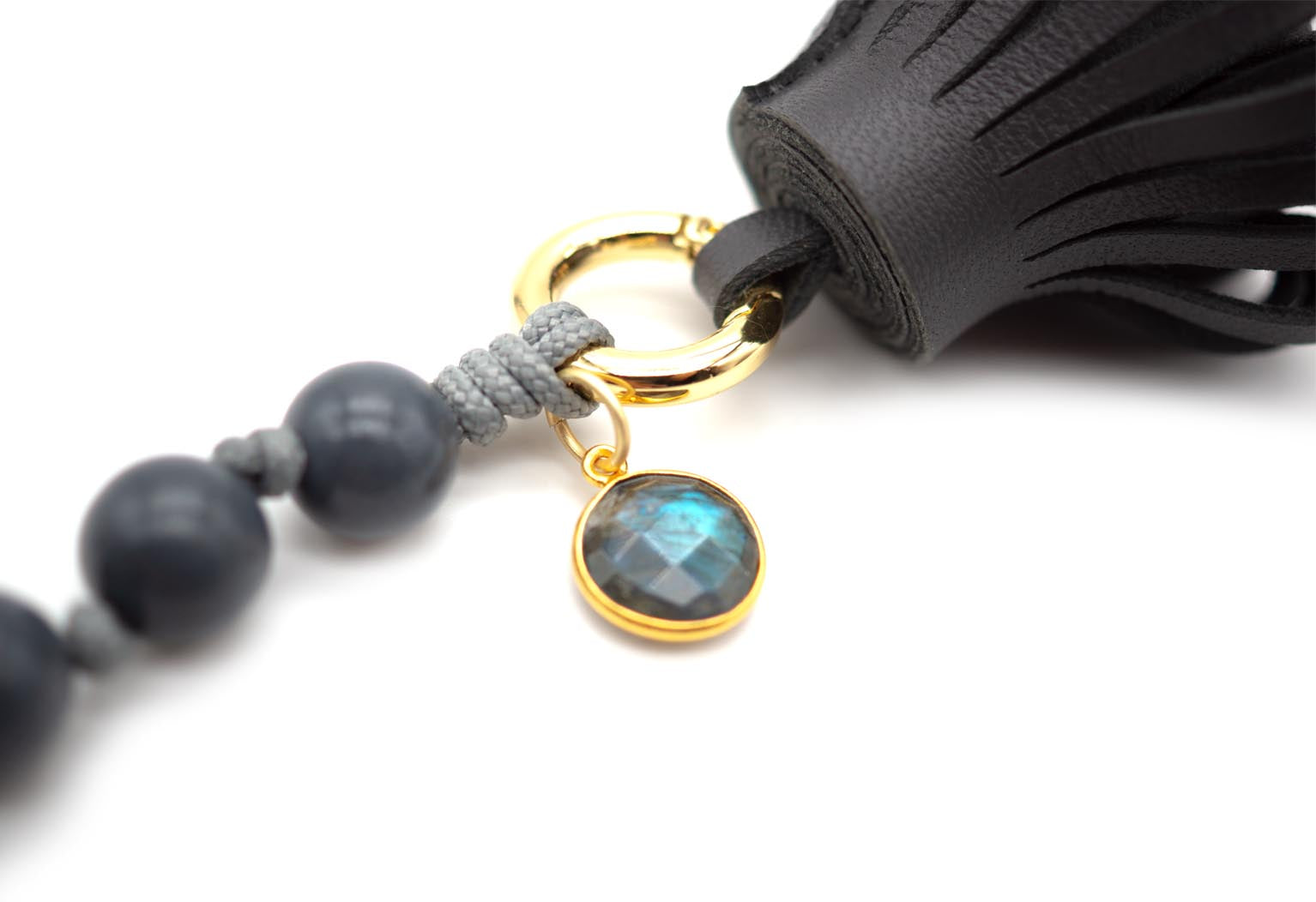 Detailansicht des vergoldeten Rings mit blau schimmerndem Labradorit-Anhänger und Lederquaste