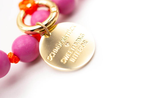 Detail des vergoldeten Logo-Tags mit Gravur am pinken Perlenstrang