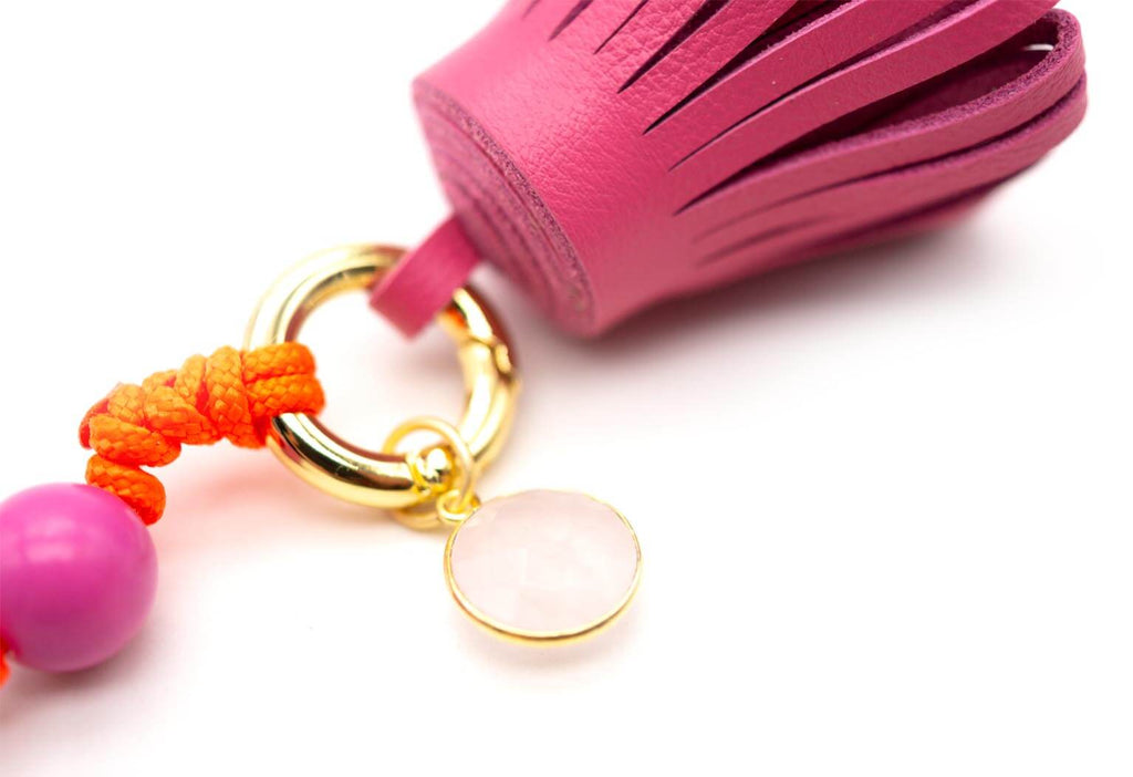 Nahaufnahme von pinker Lederquaste und rundem Rosenquarz-Anhänger am goldfarbenen Ring
