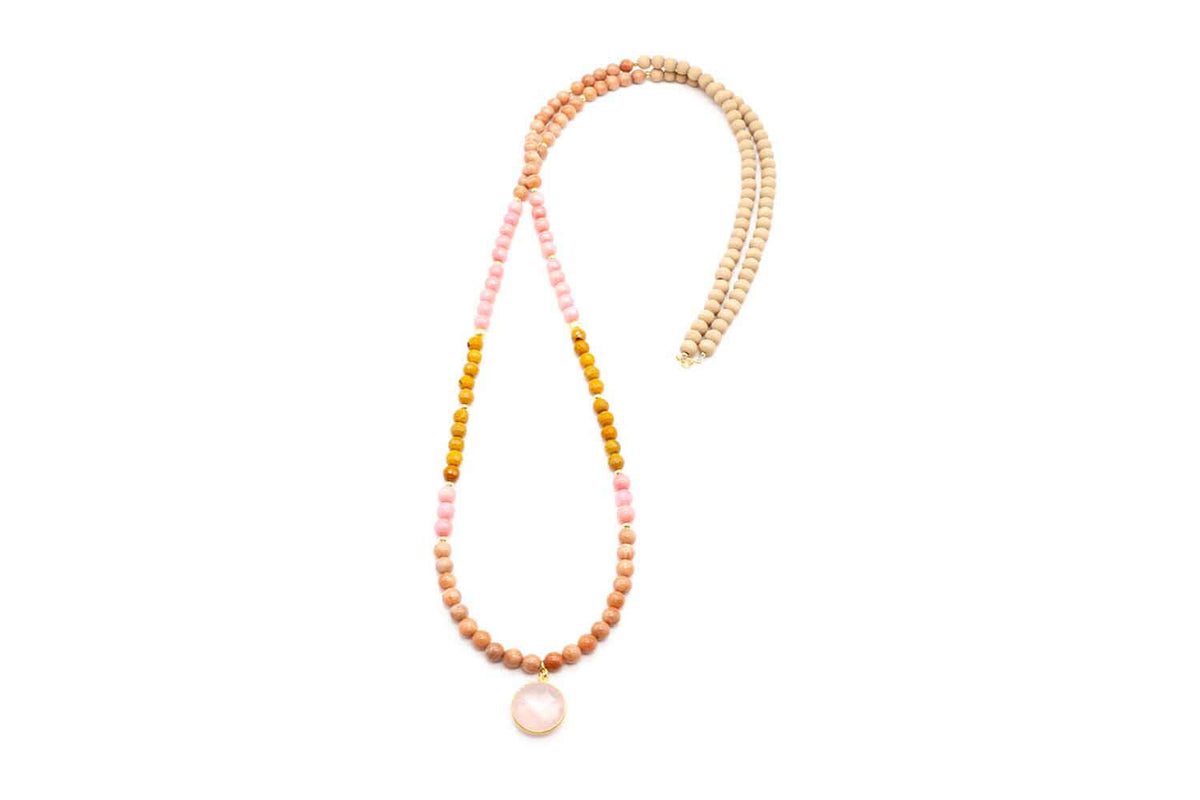 Lange Kette aus Perlen in Beige-, Rosa- und Ockertönen mit rundem Rosenquarz-Anhänger, freigestellt vor Weiß