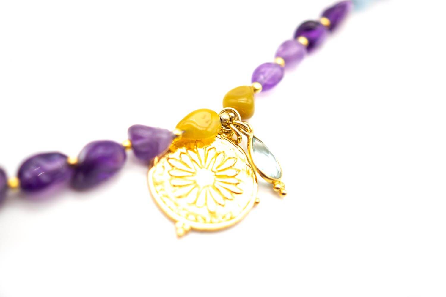 Detailaufnahme des goldfarbenen Blüten-Münzanhängers mit Aquamarin neben violetten Perlen