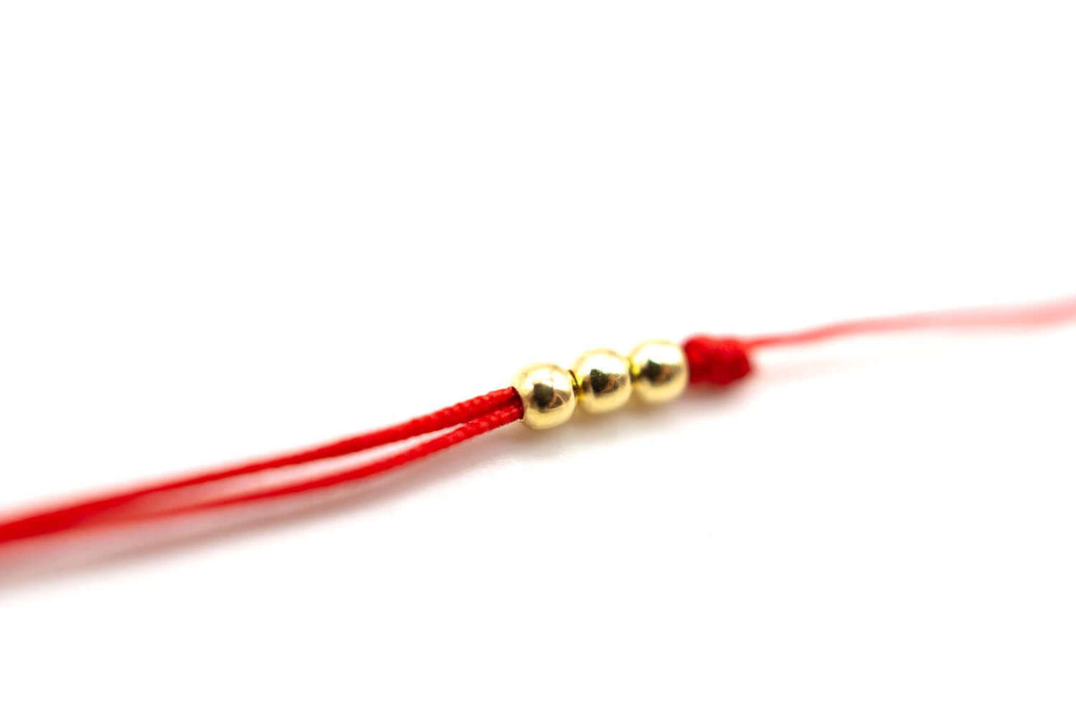 Detail des roten Nylonbands mit drei vergoldeten Perlen und Schiebeknoten
