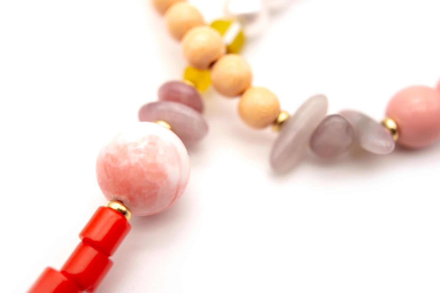 Detailaufnahme mit rosa Perle, roten Röhrchen und hellen Holzperlen