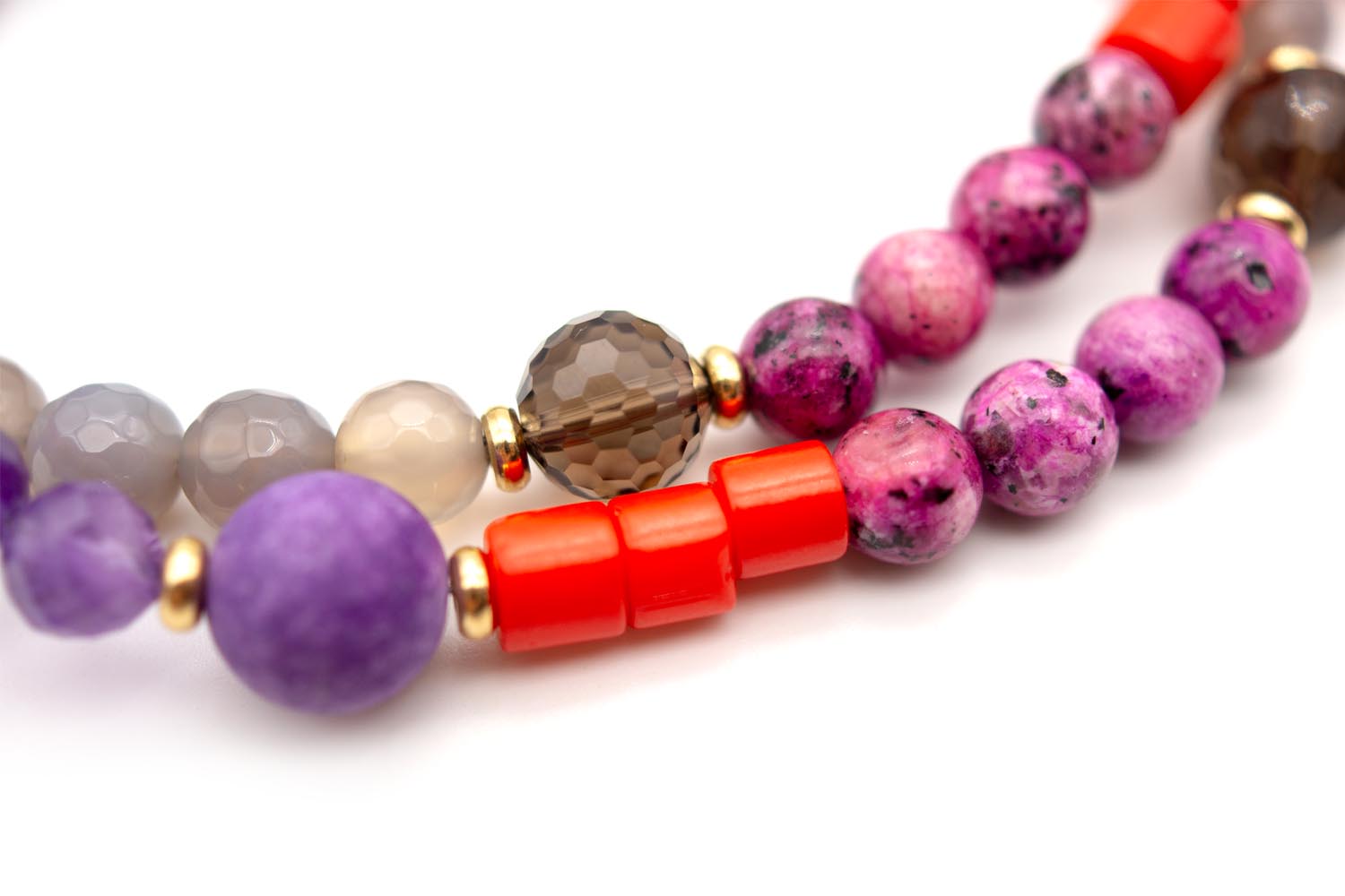 Nahaufnahme von violetten, pinkfarbenen und roten Perlen mit vergoldeten Zwischenteilen