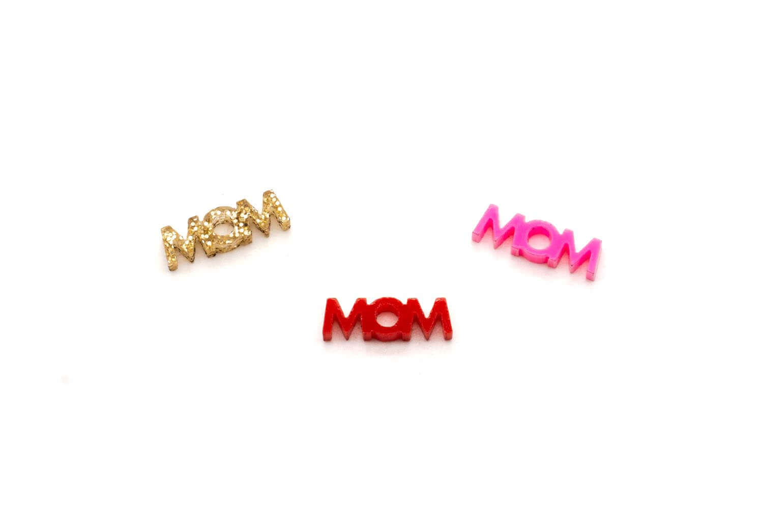 Drei Mom-Schriftzug-Anhänger aus Acryl in goldfarbenem Glitzer, Rot und Pink freigestellt