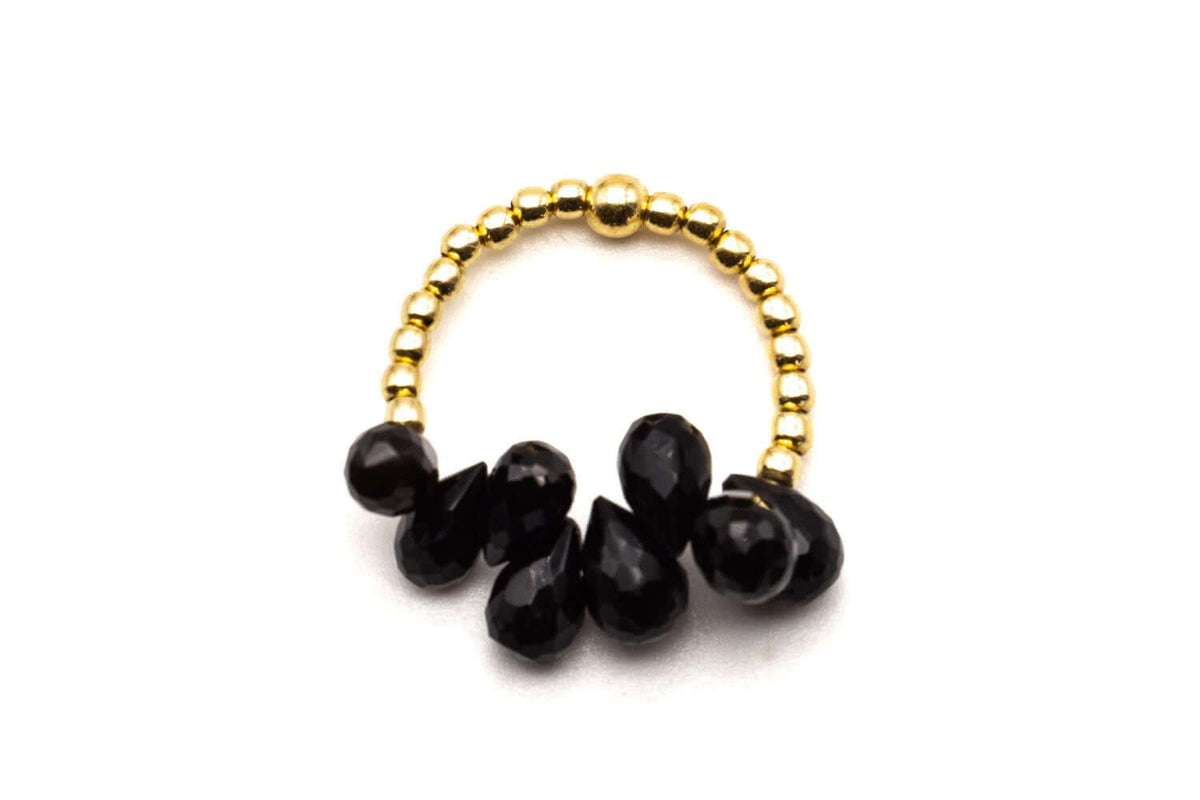 Ring aus vergoldeten Perlen auf Elastikband mit facettierten schwarzen Onyx-Tropfen, freigestellt