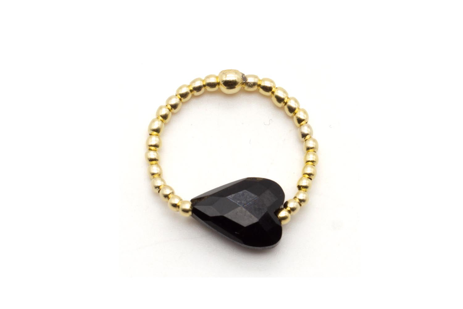 Ring auf Elastikband aus vergoldeten Perlen mit facettiertem schwarzem Onyx-Herz, freigestellt vor Weiß