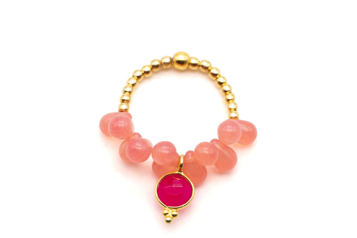 Ring auf Elastikband mit goldfarbenen Perlen, rosa Kristalltropfen und pinkem Chalcedon-Anhänger, freigestellt