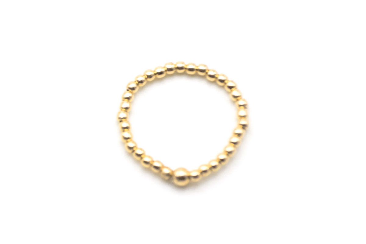 Ring aus 2mm vergoldeten Perlen auf Elastikband, freigestellt vor hellem Hintergrund